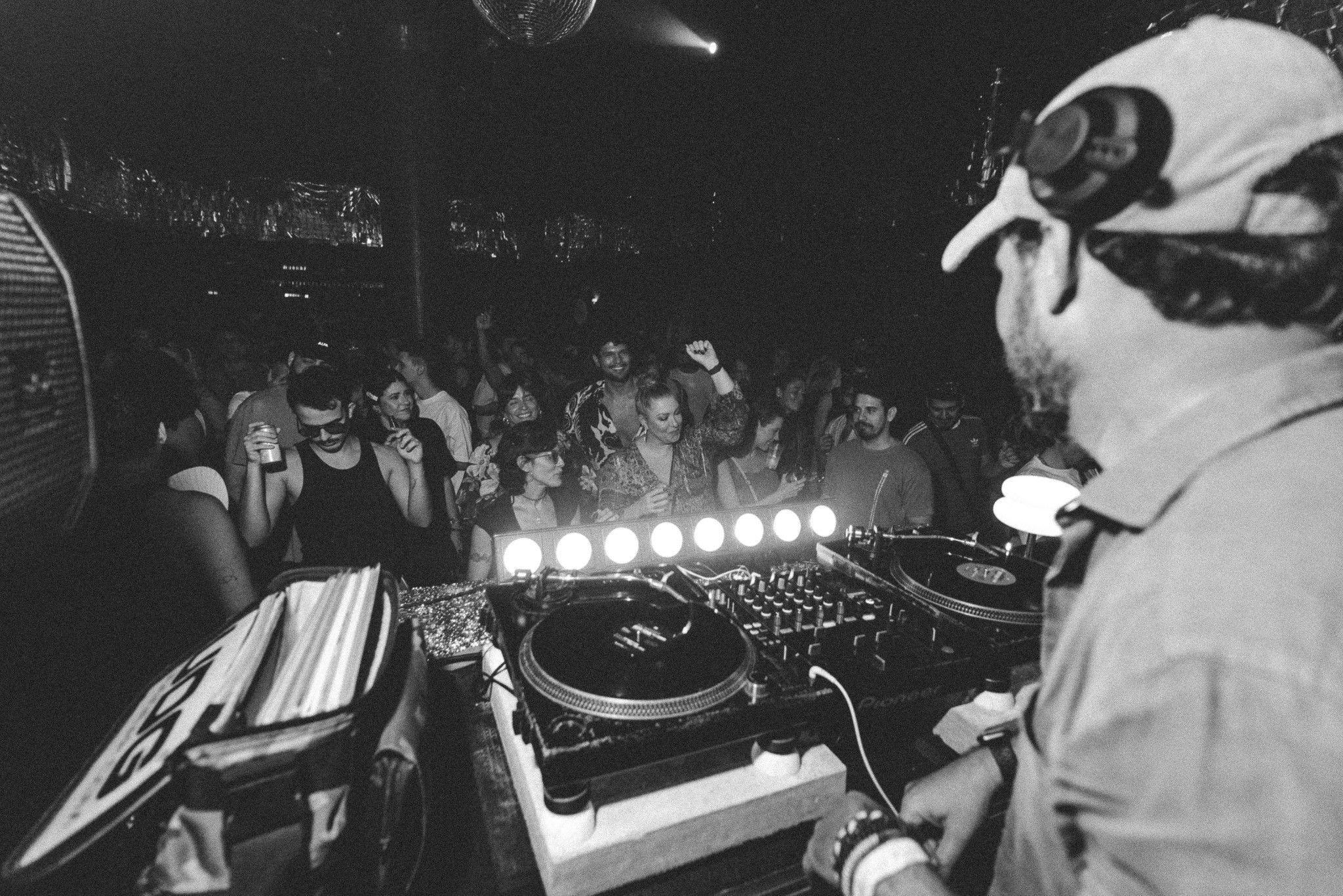 Leo Reis de boné nos toca-discos, de costas, com a pista cheia à frente