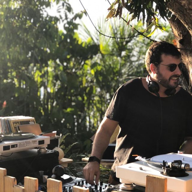 Leo Reis sorrindo entre os toca-discos brancos, ao ar livre