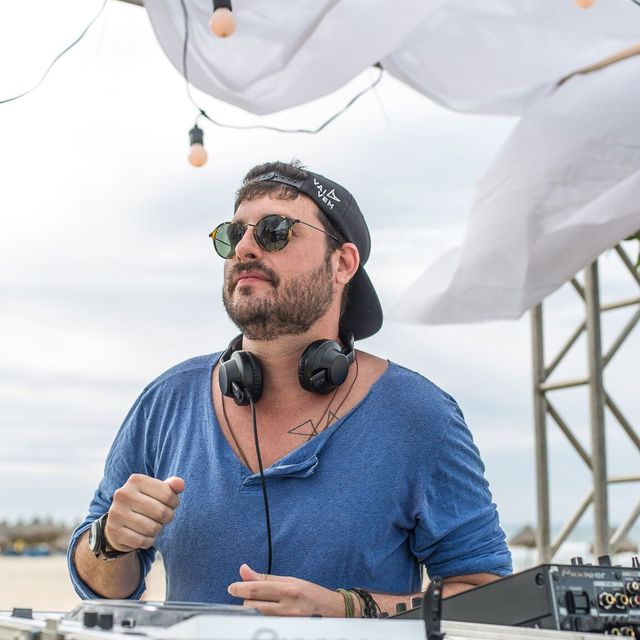 Leo Reis de óculos e boné para trás, na cabine na praia